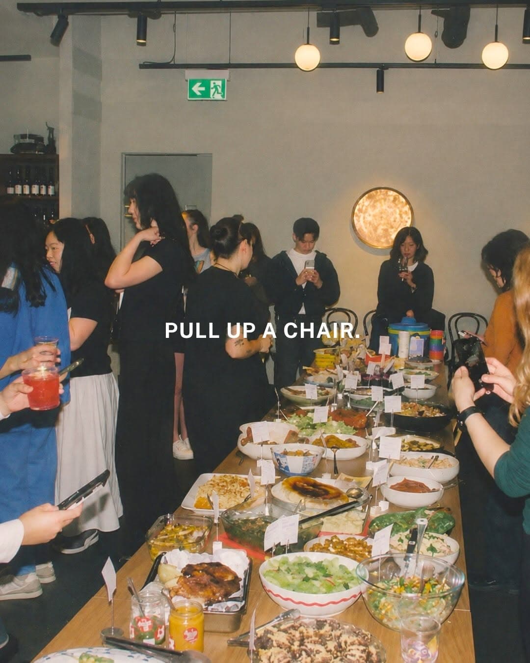 People gathering around a communal table sharing dishes cooked from recipes in a cookbook at Cookbook Club Naarm event